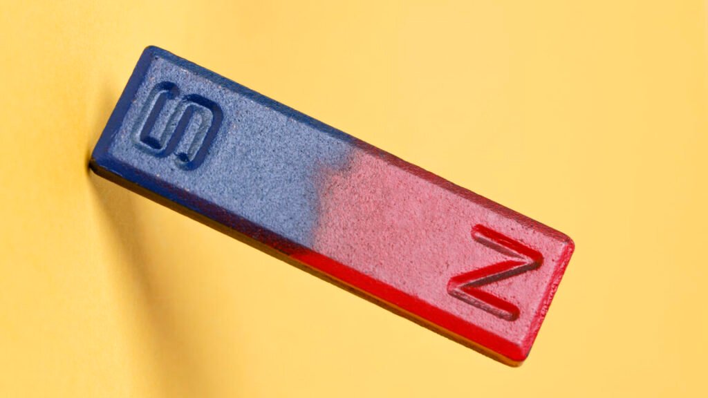 Breaking down rare earth element magnets for recycling A yellow background with a bar magnet in the foreground, with the magnetic north painted red, and the magnetic south pained blue.